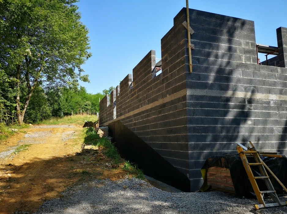 Chantier extérieur de construction, mur en parpaings (blocs béton creux) peints en noir, avec pilastres intégrés
