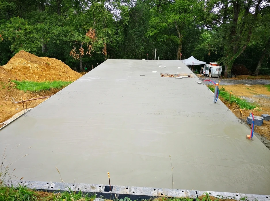 Chantier extérieur de construction résidentielle, vue aérienne d'une dalle de béton fraîchement coulée et lissée, environ 200m²