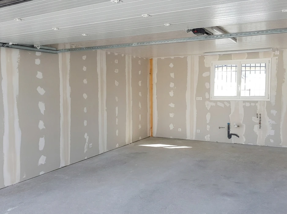Pièce en cours de construction, murs en plaques de plâtre (BA13) avec joints et enduits de lissage visibles, sol béton brut