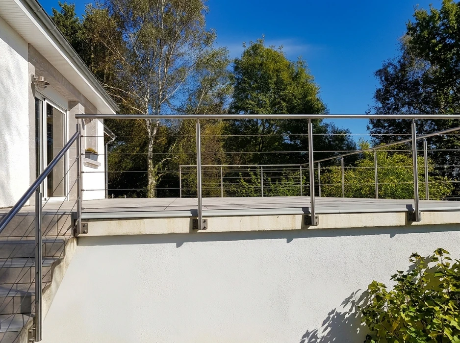 Terrasse extérieure surélevée avec lame de composite gris clair, entourée d'une garde-corps en acier inoxydable brossé à barreaux horizontaux tendus (câbles ou tiges rondes)