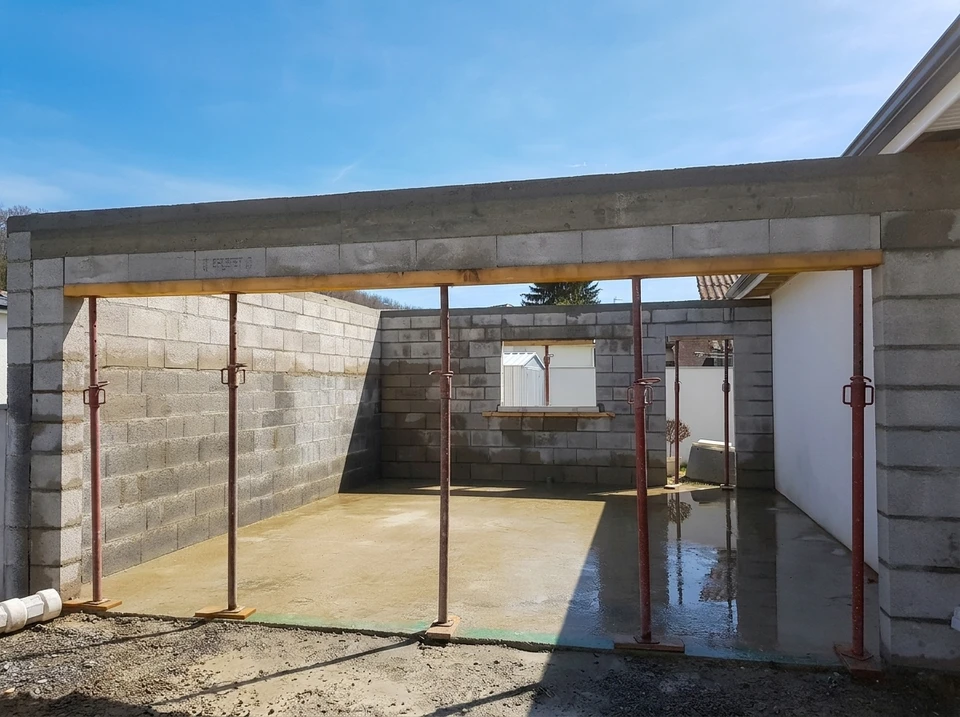 Ouvrier en équipement de protection installant un dallage extérieur, utilisant un marteau à tête jaune pour ajuster les pavés sur lit de sable